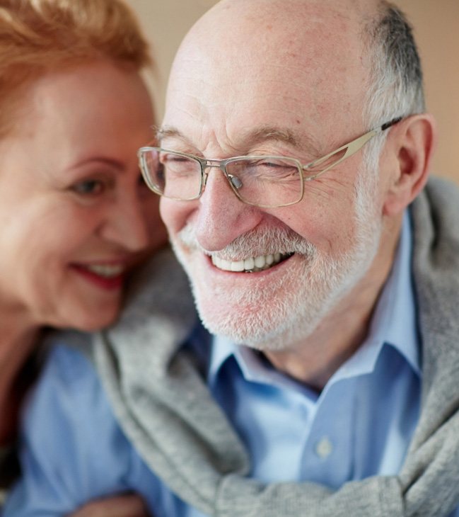 Older couple smiling after replacing missing teeth